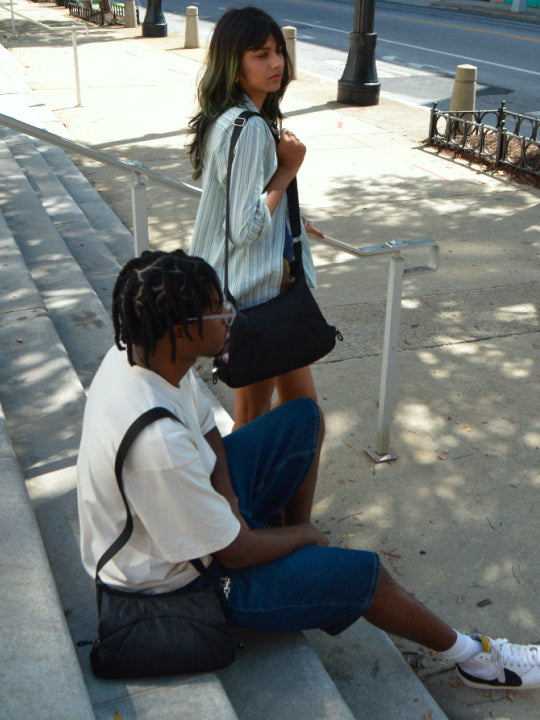 Woman sitting on concrete steps with a friend, Bottle Bag over one shoulder