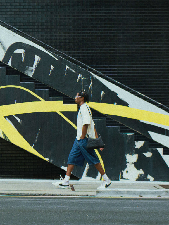 Person walking down concrete steps past a black, white and yellow mural, Bottle Bag at the hip