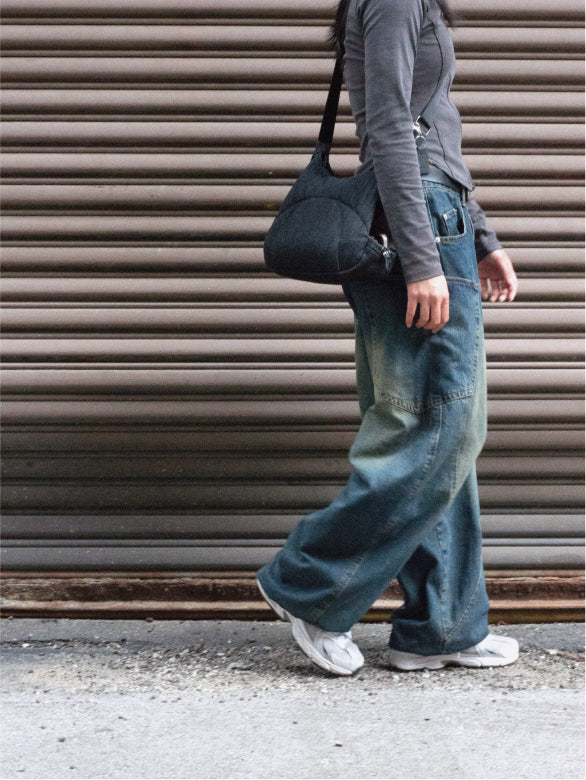 Person in wide-leg jeans walking away past a roller shutter, Bottle Bag over one shoulder